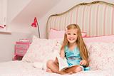Young girl sitting on bed with book smiling