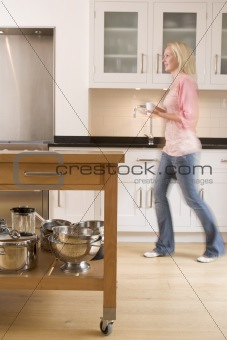 Woman walking in kitchen holding coffee