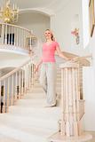 Woman coming down staircase in luxurious home smiling