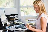 Woman in home office with computer and paperwork smiling