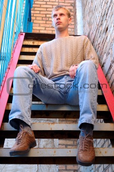 Young stylish man sit on stairs near brick wall.