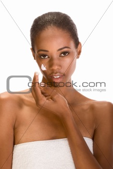 Afro-American girl wrapped in towel putting cream on face
