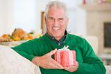 Senior Man Sitting On Sofa Holding A Christmas Gift