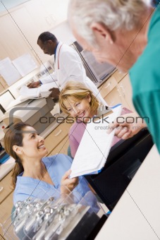 Nurses Being Handed A Clipboard At The Reception Area In A Hospi