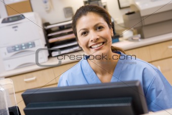 A Nurse Sitting At A Computer At The Reception Area Of A Hospita