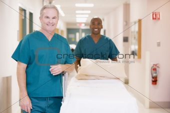 Two Orderlies Pushing An Empty Bed Down A Hospital Corridor