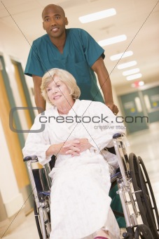 An Orderly Pushing A Senior Woman In A Wheelchair Down A Hospita