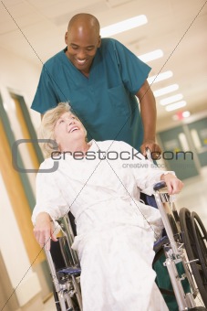 An Orderly Pushing A Senior Woman In A Wheelchair Down A Hospita