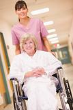 A Nurse Pushing A Senior Woman In A Wheelchair Down A Hospital C