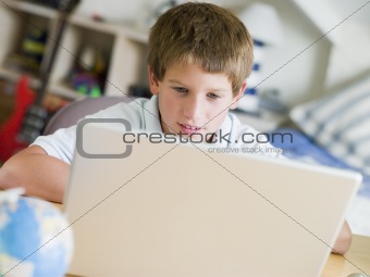 Young Boy Using Laptop In His Bedroom