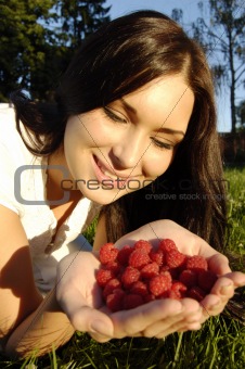 Beautiful young girl holds raspberries in hands (outdoors)