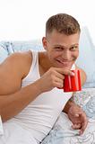 smiling male drinking coffee in bed