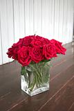 red roses in the glass vase on wooden floor