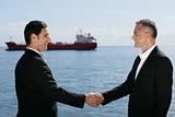 Businessmen shaking hands in front of a cargo boat