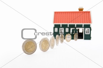 Row of euro coins rolling into a house