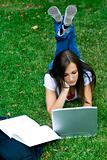 Cute teen girl laying down on the grass studying
