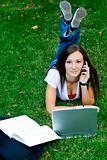 Cute teen girl on the phone laying down on the grass studying
