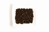 whole black pepper in square white bowl isolated