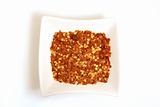 crushed chili pepper in square white bowl isolated