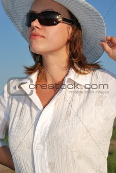 The woman in glasses and a hat on a background of the sky
