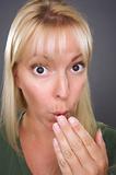 Shocked Blond Woman with Hand in Front of Mouth Against a Grey Background