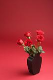 Five red roses in the vase on the red background