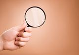Hand holding magnifying glass on the beige background