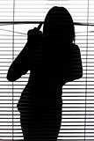 silhouette of woman looking through the blind