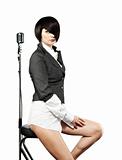 Young woman with fashion haircut sitting back to the vintage microphone, on white