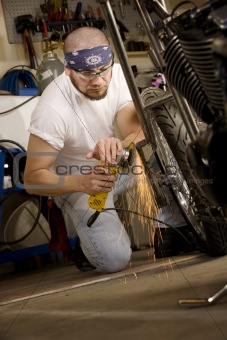 Hispanic man using grinder on motorcycle