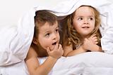 Kids playing under the quilt in bed