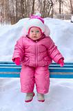 Pretty little girl in winter outerwear sit on  bench.