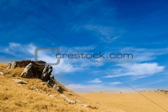 Beautiful clouds over the golden grassland and rock.