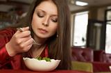 Beautiful brunette girl in red eats salad.