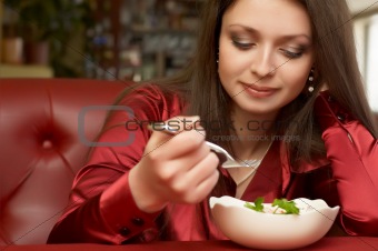 Beautiful brunette in red eats salad.