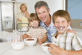 Father With Children As They Eat Breakfast And Mother In The Bac
