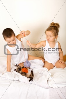 Kids playing with their kitten on the bed