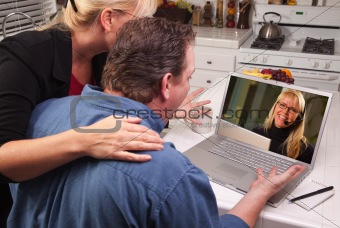 Couple In Kitchen Using Laptop with Customer Support Woman on the Screen.