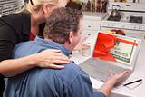 Couple In Kitchen Using Laptop with Stack of Money Wrapped in a Red Ribbon on the Screen.