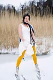 Woman wearing a stylish dress, scarf and ice skates standing on a frozen lake.
