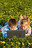 Kids using laptop on the spring flower field