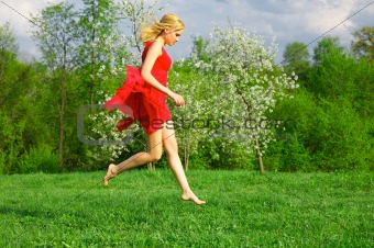Young beautiful woman in a red dress jumping on lawn