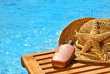 Suntan lotion and straw hat by the pool