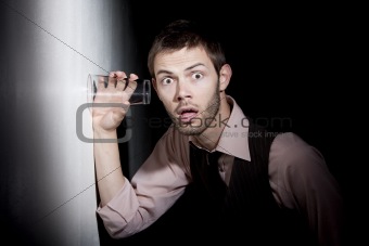 Handsome young man using glass to eavesdrop