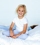 Little girl in bed smiling at the camera while her brother is sl