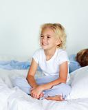 Little girl in bed smiling while her brother is sleeping