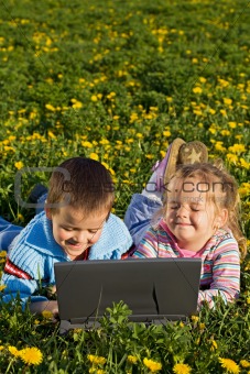Two kids outdoors having fun with a laptop