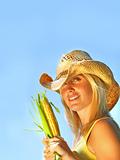 Pretty young woman holding corn against blue sky
