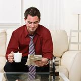 Attractive male drinking coffee and reading a newspaper