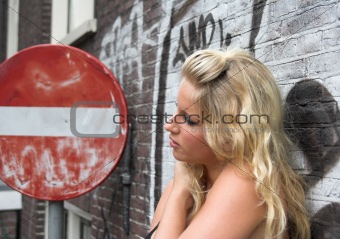 Attractive blonde standing next to a red road sign